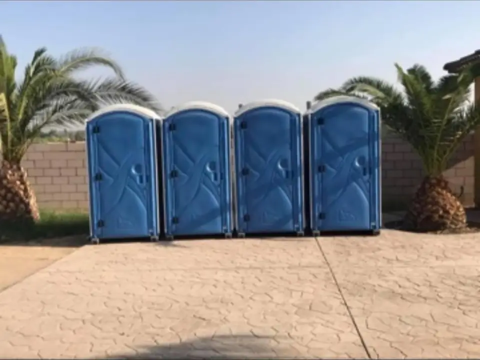 Four blue porta potties lined up on a paved lot