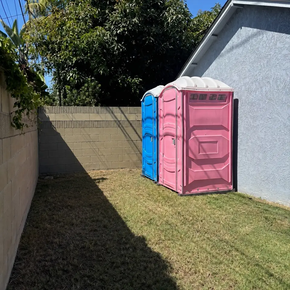 Pink and blue porta potties in a fenced backyard on grass
